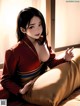 A woman in a red kimono sitting on a bed.