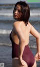 A woman in a maroon one piece swimsuit standing on the beach.