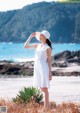 A woman in a white dress and hat standing on a beach.