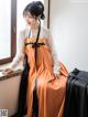 A woman in an orange and black hanbok sitting on a window sill.