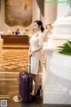 A woman in a white dress with a purple suitcase.