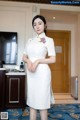 A woman in a white dress standing in a hotel room.