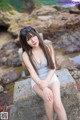 A woman sitting on a rock by the water.