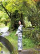 A woman in a blue and white kimono standing next to a stream.