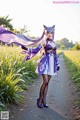 A woman in a purple and white dress standing on a dirt road.