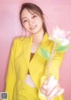 A woman in a yellow suit holding a flower.