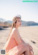 A woman in a pink dress sitting on a beach.