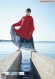 A woman in a red sweater is standing on a concrete wall by the water.