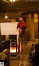 A woman in a red shirt and panties standing in a living room.