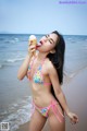 A woman in a bikini eating an ice cream cone on the beach.