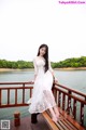 A woman in a white dress sitting on a wooden bridge.