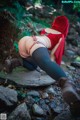 A woman in a red hooded outfit is bending over on a rock.