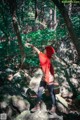 A woman in a red hoodie standing on a rock in the woods.