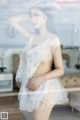 A woman in a white lingerie posing in front of a window.