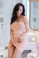 A woman in a pink dress sitting on a bathroom counter.