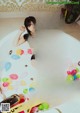 A woman sitting in a bathtub surrounded by balloons.