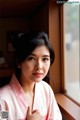 A woman in a pink kimono leaning against a window.